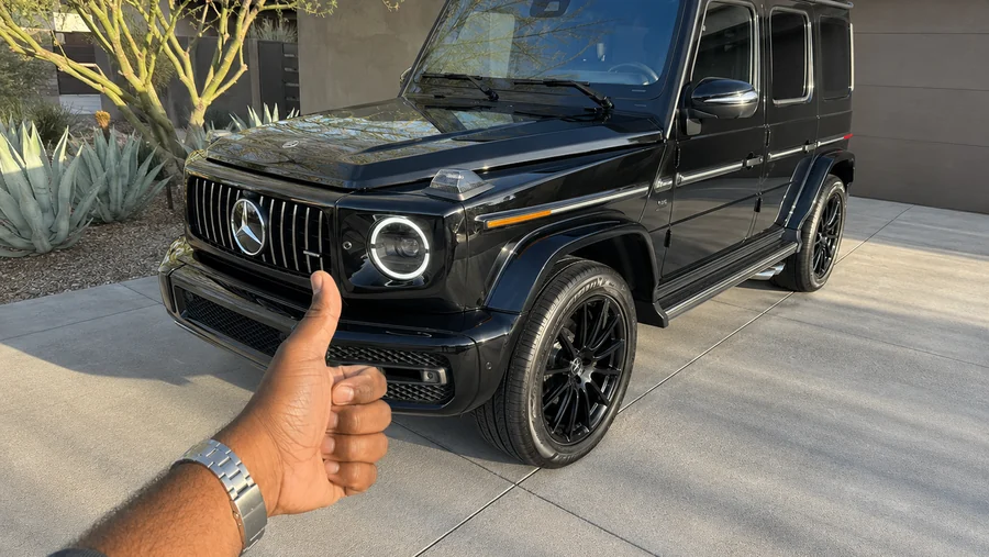A customer giving a thumbs up next to his freshly detailed black Mercedes G-Wagon in the driveway